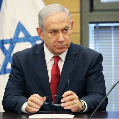 Benjamin Netanjahu ser fundersam ut med Israels flagga i bakgrunden.