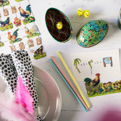 Ett bord fullt med påskrelaterade prylar: ett kort med en tupp, två påskägg, ett glas med mjöd och några påskkvistar.