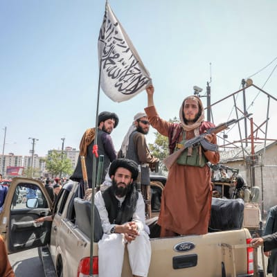 Talibaner sitter på ett bilflak och håller upp en flagga.