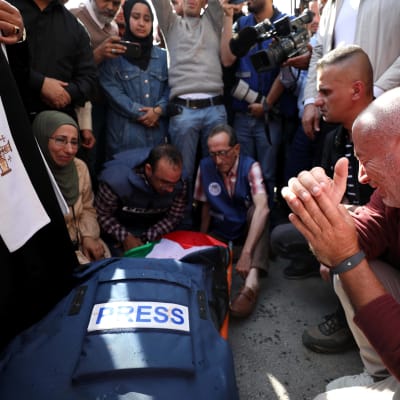 Journalisten Shireen Abu Akleh som dödats av israeliska soldater ligger på marken med journalistväst och den palestinska flaggan ovanpå.