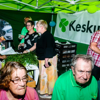 Annika Saarikko står i ett Centern-tält på ett torg och diskuterar med väljare.