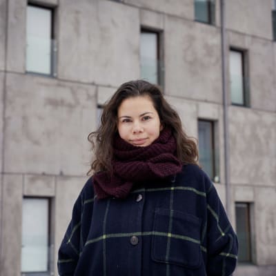 Liza Alexandrova-Zorina står framför en betongfasad. Hon har en rutrandig jacka och en halsduk på sig.