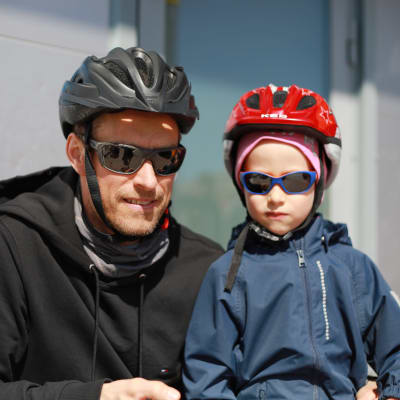 En man och en liten pojke, båda med solglasögon och cykelhjälm, tittar in i kameran