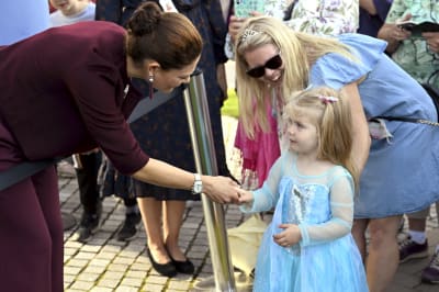 Kronprinsessan Victoria hälsar på en liten blond flicka i ljusblå prinsessklänning.