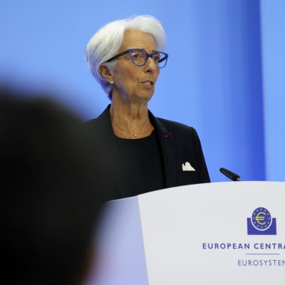 Christine Lagarde klädd i svart talar vid ett podium med texten European Central Bank - Eurosystem. I förgrunden syns huvuden av personer i publiken.
