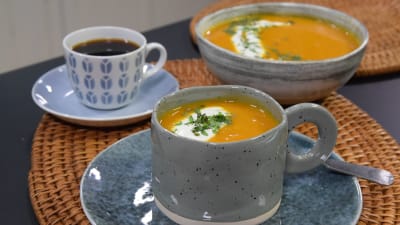 Portioner med morotsoppa och en kopp med kaffe på ett bord
