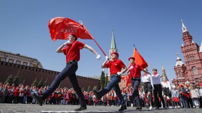 Tre rödklädda unga marscherar med en flagga i handen.