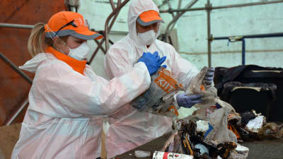 Bild av två personer i skyddsutrustning som sorterar sopor. 