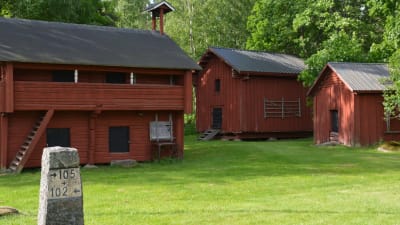 Gamla lador och gårdsbyggnader i stock och målade med rödmylla på en gård. Sommar.