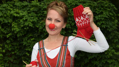 Kvinna med clownnäsa håller upp halvföärdigt stickad socka