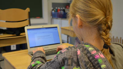 En flicka sitter i en skolbänk och skriver på sin lärplatta.