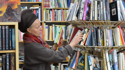 En kvinna står omgiven av böcker och sorterar böcker som är uppradade i en rund ställlning