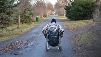 En person i rullstol åker fram på en smal väg eller gångväg i höstlandskap. 