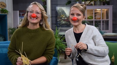 Två kvinnor med clownnäsor sitter i soffan och stickar