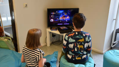 Två barn spelar tv-spel och har ryggarna svängda mot kameran.