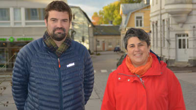 en man i blå dunrock och en kvinna i röd jacka står ute på Rådhustorget i Ekenäs. De ser mot kameran och ler.