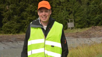 En man med orange keps och gul skyddsväst. Står  ute på en åker som ska bli våtmark.
