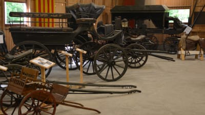 Gamla vagnar och skrindor  i ett museum. I bakgrunden också en gammal likvagn.