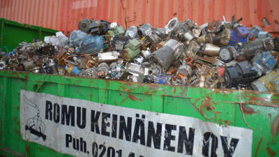 Metallskrot i en grön container. Det stor Romu Keinänen på containern.
