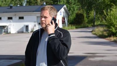 en man står utomhus och pratar i mobiltelefon. Sommar.
