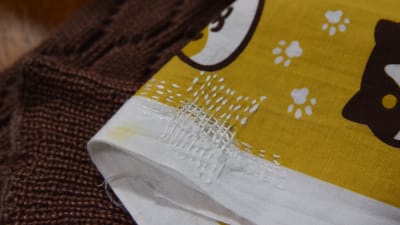 En japansk handduk med animerat tryck som föreställer katter och spår av tassar. Handduken är lagad med sashiko-stygn.