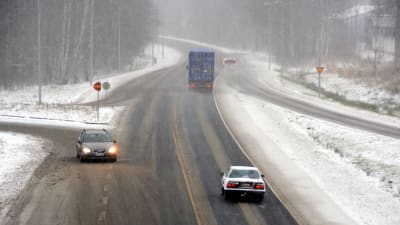 Bilar kör på en väg som är täcks med slask. Snön yr.