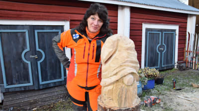 Konstnären Ulla Haglun lutar sig mot sin skapelse, en träskulptur-tomte.