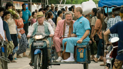 Allan (Robert Gustafsson) kör en moped genom en folkmängd, i sidovagnen sitter Julius och Gäddan.