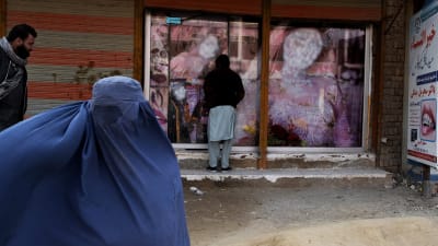 Burkhaan pukeutunut nainen kävelee Jalalabadin kaupungissa ohi näyteikkunan, jossa näkyvän naisen kuvan kasvot on peitetty maalilla.