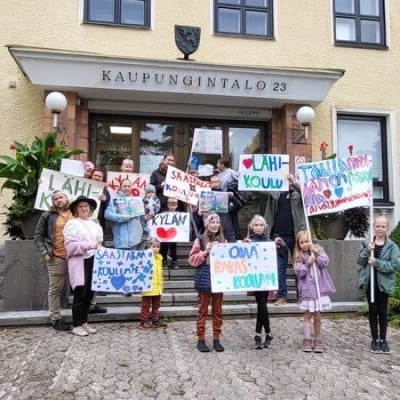 Yhteensä 15 lasta ja aikuista seisoo kaupungintalon portailla mielenosoituskylttien kanssa.