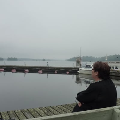 Nainen istuu penkillä järven rannalla. 