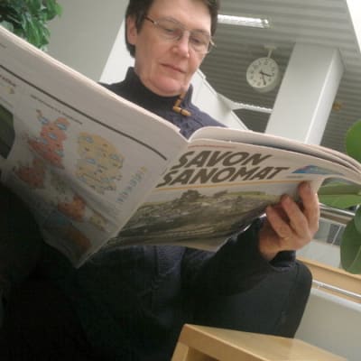 Nainen selaa tabloidikokoista sanomalehteä.