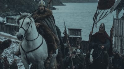 En vikingakung rider in i staden på sin vita häst, flankerad av sina män.