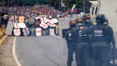 Polis med kravallsköldar och vattenkanoner står mittemot tusentals demonstranter som söker skydd bakom fanersköldar på en motorväg i Caracas.
