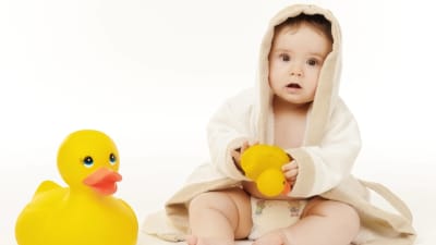 En babys i badkappa med en gul badanka i handen.