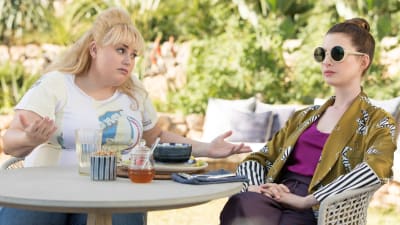 Penny (Rebel Wilson) och Josephine (Anne Hathaway) sitter vid ett bord i trädgården och argumenterar.