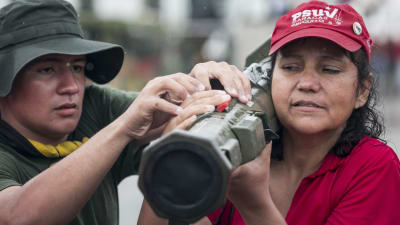 En kvinna håller i ett vapen på sin axel medan en man hjälper till i Caracas den 26 augusti. Både militära och civila deltog i Venezuelas militärövning.