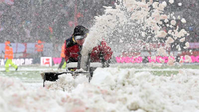 Personal vid fotbollsarenan i Köln röjer snö från planen. 