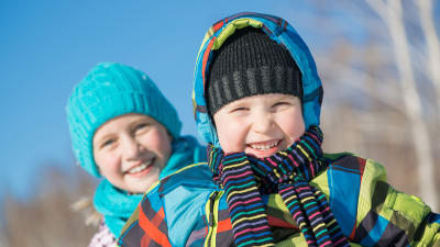 En pojke och en flicka i vinterkläder skrattar mot kameran
