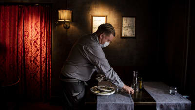 En servitör plockar ihop kärl från ett bord i en mörk restaurang.