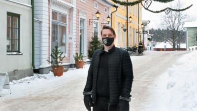 En man står i vintrigt Gamla stan i Borgå, han har svart munskydd på sig.
