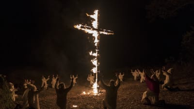 Ku Klux Klan-medlemmar knäböjer inför ett brinnande kors.
