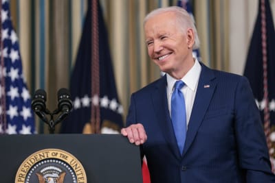 USA:s president Joe Biden som ler vid ett podium.