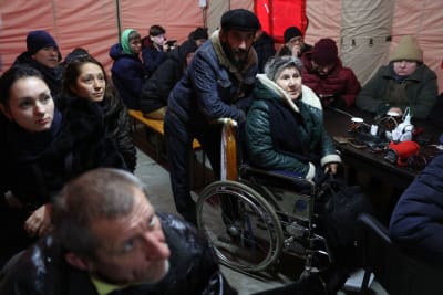 Människor lyssnar på försvarsadministrationens chef i Cherson i ett mobilt värmetält. En man står bakom en äldre kvinna i rullstol i mitten av bilden.