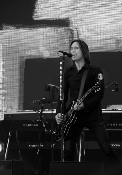 Svartvit bild på Per Gessle som spelar gitarr och sjunger i mikrofon.