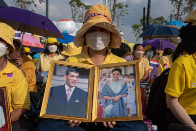 Thailändska rojalister klädda i gula skjortor håller upp  en bild av kung Maha Vajiralongkorn ( Rama X) and drottning Suthida.
