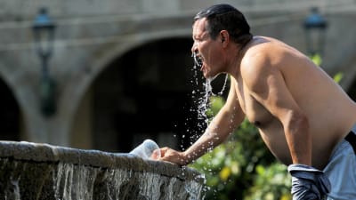 En man utan skjorta häller vatten över sig från en fontän.