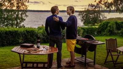 Frej (Tom Rejström) och Alex (Wilhelm Enckell) står i en trädgård vid en grill och ser ut mot havet.