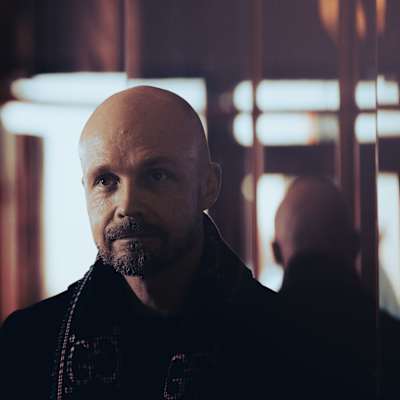 Juha Tapio kuvattuna ruskeasävyisessä huoneessa peilin edessä, musta takki yllään.