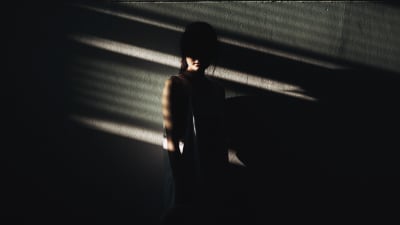 Ung kvinna lutar mot en vägg i mörker